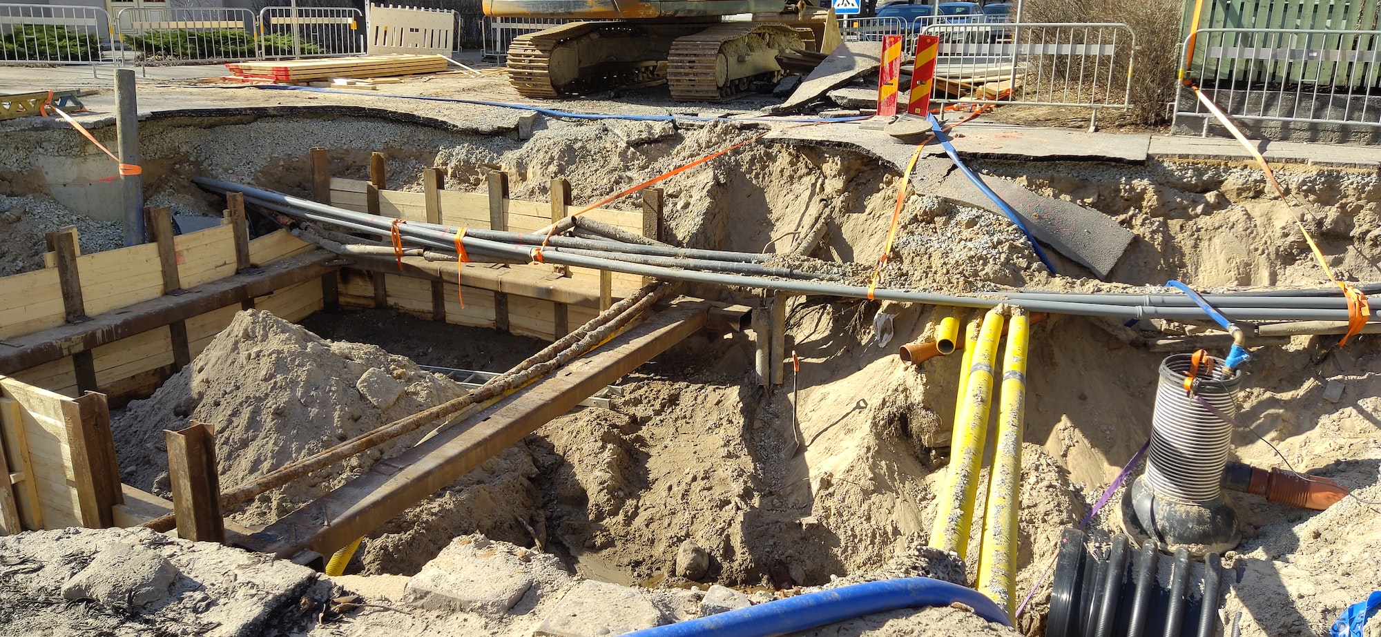 Many multicolored plastic pipes are in a trench of sand in perspective